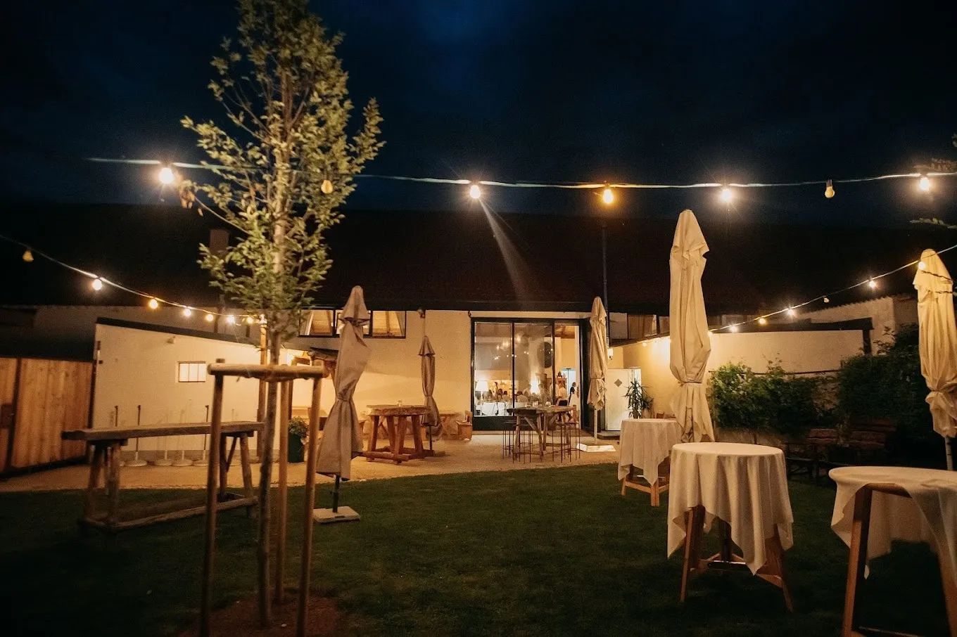 Weingut Artner courtyard at night with string lights, cocktail tables, and the lit interior visible through glass doors