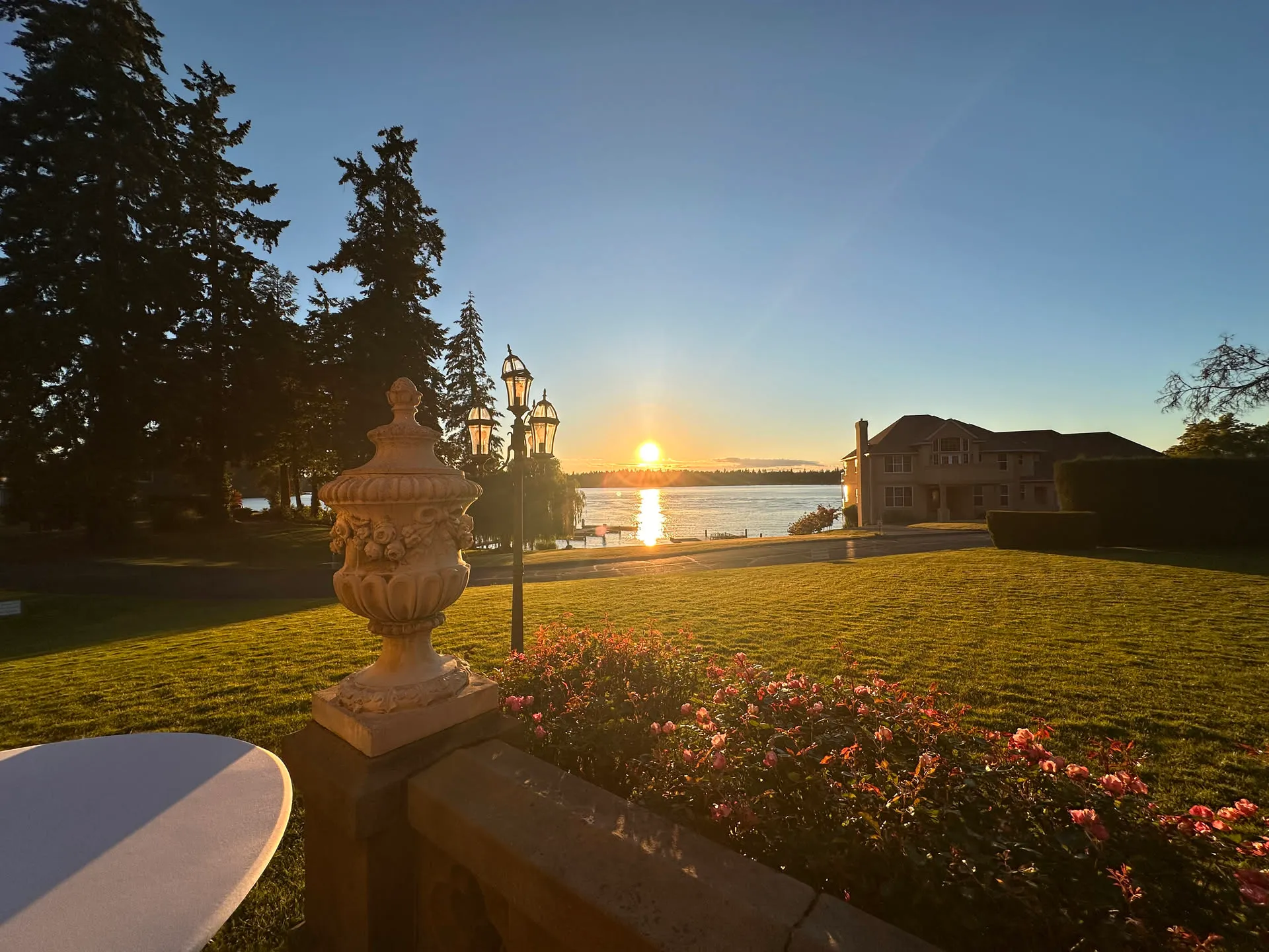 Sunset over American Lake behind Thornewood, framed by a stone urn and flower beds