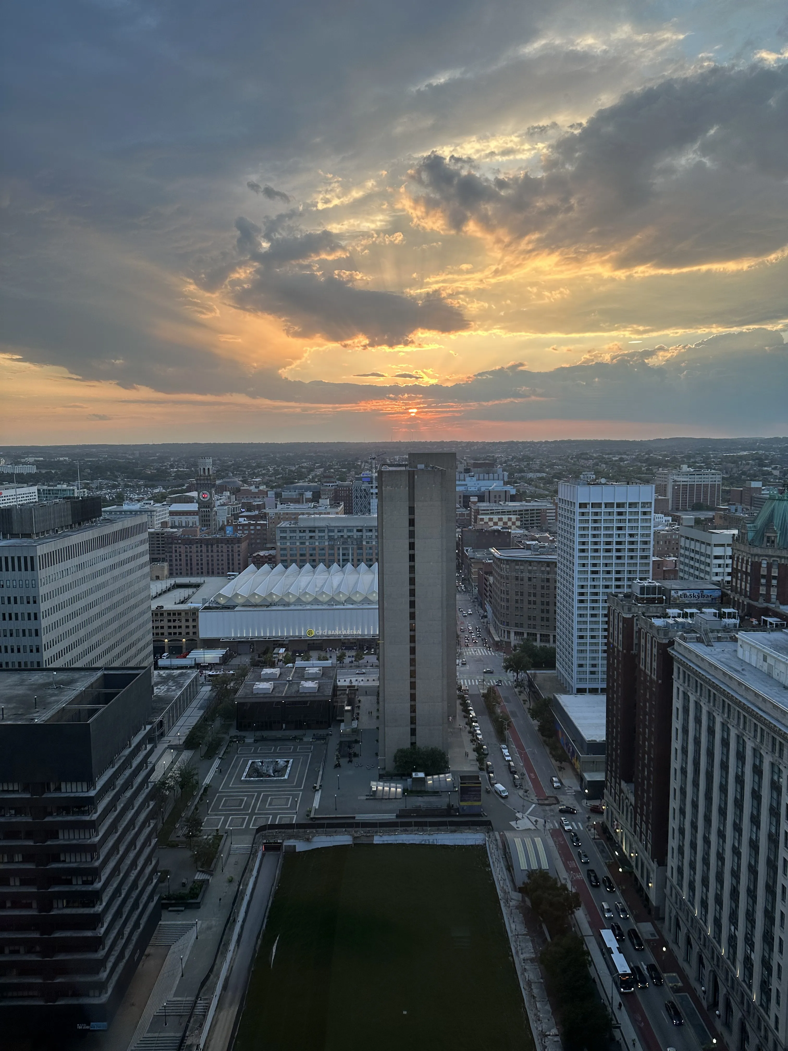 Sunset over Baltimore from a downtown high-rise, with sun rays breaking through clouds and M&T Bank Stadium visible to the left