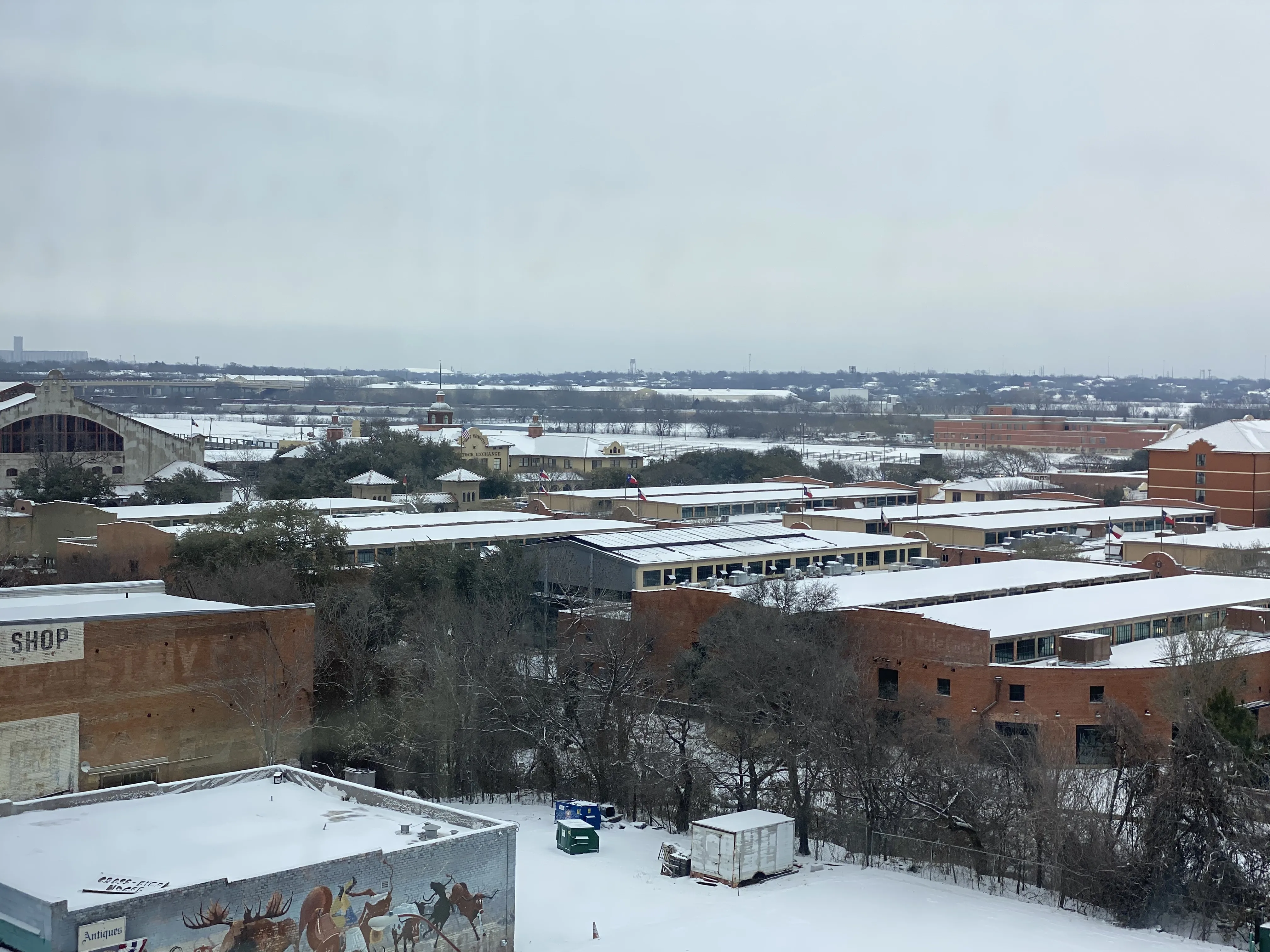 Snow over Fort Worth rooftops with the downtown skyline beyond