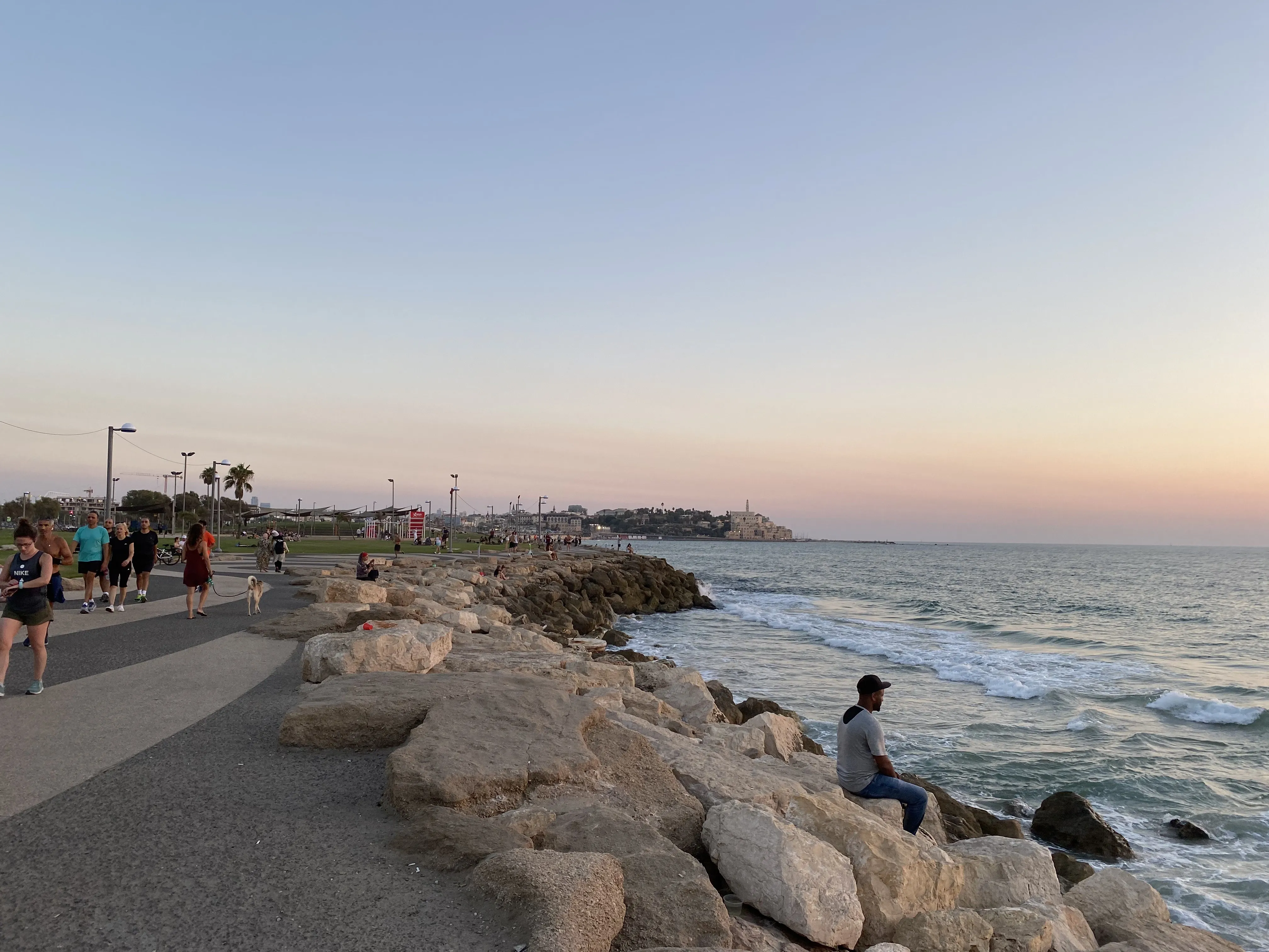 Tel Aviv beach at dusk with rocks and people walking the shore